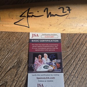 May include: A wooden baseball bat with a signature and the number 27. A JSA authentication certificate is included, with the certification number CE15207. The certificate features images of signed memorabilia.
