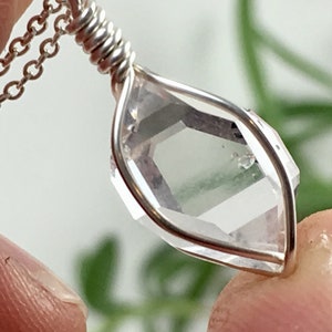 May include: A silver chain necklace with a clear quartz crystal pendant wrapped in silver wire.