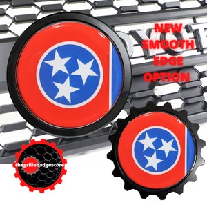 May include: Two black and red Tennessee state flag car emblems. One emblem has a smooth edge and the other has a gear-like edge. The text "NEW SMOOTH EDGE OPTION" is visible in the background.