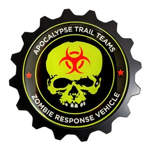 May include: Black, gear-shaped emblem with the text "APOCALYPSE TRAIL TEAMS" and "ZOMBIE RESPONSE VEHICLE". The center features a neon green skull and biohazard symbol on a black background. Red star accents.