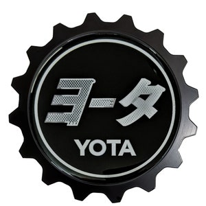 May include: Black and silver metal emblem with a gear design. The emblem features the Japanese word "Yota" in silver lettering and the word "YOTA" in white lettering.