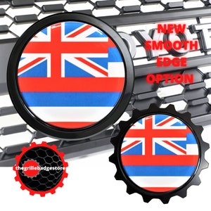 May include: Two black and white car grille emblems with the Hawaiian flag. The emblems are round with a smooth edge option. The text "NEW SMOOTH EDGE OPTION" is visible in the background.