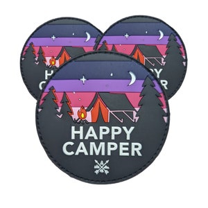 May include: Three black round patches with a colorful camping scene and the text "Happy Camper" in white. The scene features a tent, a campfire, and trees against a pink, purple, and blue sunset.