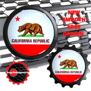 May include: Two black metal car emblems with a red, white, and blue California state flag design. The flag features a red star and a brown bear walking on green grass. The text "CALIFORNIA REPUBLIC" is printed in black on the flag. The emblems are on a black and gray background. "NEW SMOOTH EDGE OPTION" is printed in white on the background.
