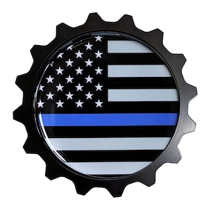 May include: Black and white American flag with a blue stripe across the middle, displayed on a black gear-shaped emblem.
