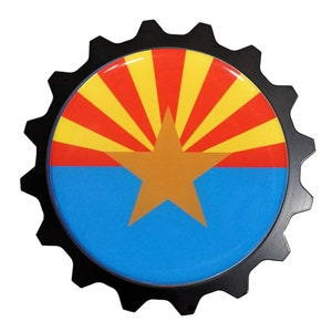 May include: A black gear-shaped emblem with a red, yellow, and blue Arizona state flag design. The flag features a gold star in the center.