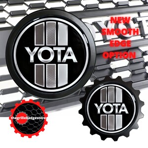 May include: Black and silver YOTA logo emblem with a smooth edge option. The logo is on a black round base and a black gear-shaped base. The logo is surrounded by a black and gray grille.