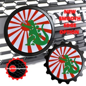May include: Two black and red car emblems with a white background. The emblems feature a green Godzilla-like creature holding a wrench in front of a red and white rising sun design. The text "NEW SMOOTH EDGE OPTION" is visible in the background.
