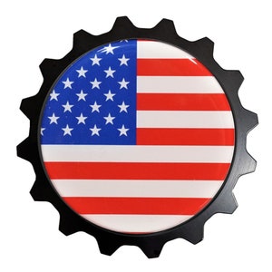 May include: A black metal gear-shaped emblem with a red, white, and blue American flag design in the center.