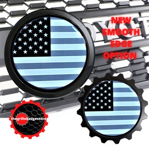 May include: Two black metal car emblems with a blue and white American flag design. The larger emblem is round and the smaller emblem is shaped like a gear. The text "NEW SMOOTH EDGE OPTION" is visible in the background.