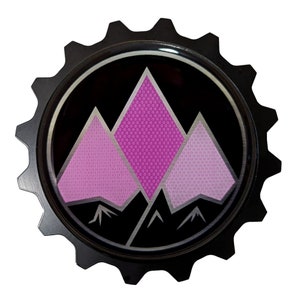 May include: A black metal gear-shaped emblem with a pink mountain design. The mountains are stylized and have a textured pattern.