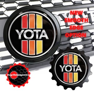 May include: Two black car emblems with a silver YOTA logo and red and yellow stripes. The emblem on the left has a smooth edge, while the emblem on the right has a serrated edge. The text "NEW SMOOTH EDGE OPTION" is visible in the background.