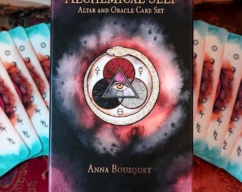 May include: The Alchemical Self Altar and Oracle Card Set by Anna Bousquet features a black box with a central circular illustration of a snake eating its tail, a triangle with an eye, and alchemical symbols, surrounded by cards with similar art.