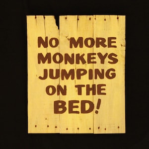 Peut inclure: Une pancarte en bois jaune avec le texte "NO MORE MONKEYS JUMPING ON THE BED!" peint en lettres brunes.