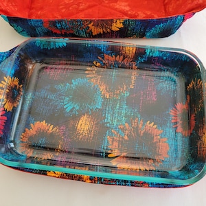 May include: A glass baking dish with a blue, orange, and pink floral pattern on the outside. The dish is sitting on a red and blue floral fabric.