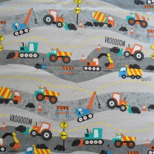 May include: A gray fabric featuring a repeating pattern of construction vehicles, including trucks, excavators, and tractors. The design incorporates road signs, orange traffic cones, and the text "VROOOOOM" and "BEEP BEEP". The vehicles are in shades of orange, blue, and green.