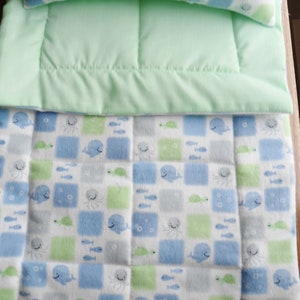 May include: A green and white baby blanket with a blue whale, octopus, and fish pattern. The blanket is made of soft, plush fabric and is perfect for cuddling.
