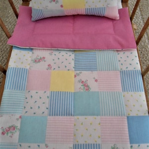 May include: A patchwork doll bed quilt with a pink, yellow, blue, and white color scheme. The quilt is made of different fabrics with floral and striped patterns.