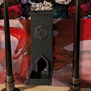 May include: Three black candlesticks with lit candles stand in front of a miniature stone fireplace. The candlesticks are on a black and white chequered surface. The background is a white fabric with a repeating pattern of colourful dice.