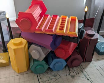 May include: A collection of colorful, geometric storage containers in various shapes and sizes. The containers are in shades of red, pink, yellow, purple, gray, green, blue, and brown. Some have lids, and others have open compartments.
