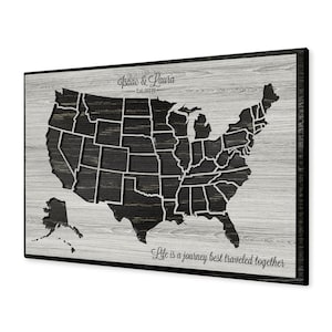 May include: A wooden map of the United States with a black and white color scheme. The map is framed in black and has the text "Isaac & Laura - Est. 2019" at the top and "Life is a journey best traveled together" at the bottom.
