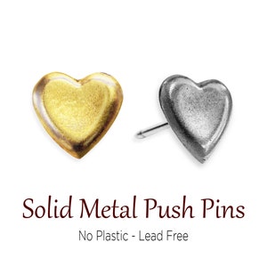 May include: Two heart-shaped push pins. One is gold-colored, the other is silver. The pins are made of solid metal and are lead-free. The text "Solid Metal Push Pins" and "No Plastic - Lead Free" is below the pins.
