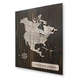 May include: A wooden map of North America with a compass and the text "Adventure Awaits". The map is carved into a dark wood background with a light wood overlay.