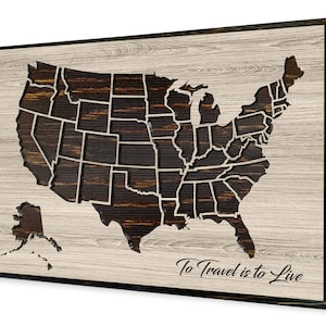 May include: A wooden wall art piece featuring a map of the United States with each state outlined. The map is carved into the wood and has a dark brown finish. The background is a light wood color. The text "To Travel is to Live" is written below the map.