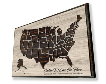 May include: A wooden wall art piece featuring a laser-cut map of the United States with each state outlined. The map is on a light wood background with a dark wood frame. The text "Custom Text Can Go Here" is printed below the map. Add Names & Dates - Multiple Fonts To Choose From