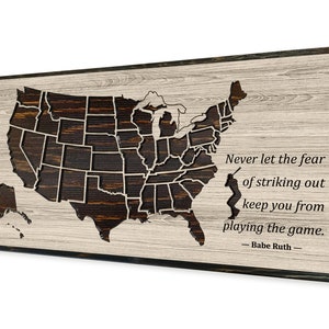 May include: Wooden wall art featuring a detailed map of the United States with a dark brown finish, set against a light wood grain background. The artwork includes a quote by Babe Ruth and a silhouette of a baseball player.