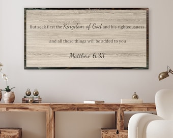 May include: A rectangular wooden sign with a black frame displays the text "But seek first the Kingdom of God and his righteousness and all these things will be added to you Matthew 6:33". The sign is mounted on a light-colored wall.