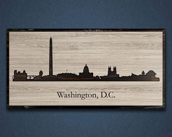 May include: A wood sign with a black silhouette of the Washington, D.C. skyline, including the Washington Monument, the Capitol Building, and other landmarks. The text "Washington, D.C." is printed below the skyline.