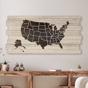 May include: A wooden wall art piece featuring a cutout map of the United States with each state outlined. The map is dark brown and the wood background is light brown.