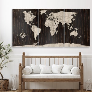 K&ouml;nnte beinhalten: Eine dreiteilige Weltkarte aus Holz an der Wand mit Kompass-Design. Die Karte ist hellbraun und der Hintergrund dunkelbraun. Die Karte ist an einer wei&szlig;en Wand &uuml;ber einer Holzbank mit wei&szlig;en Kissen angebracht.