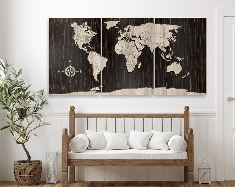 K&ouml;nnte beinhalten: Eine dreiteilige Weltkarte aus Holz an der Wand mit Kompass-Design. Die Karte ist hellbraun und der Hintergrund dunkelbraun. Die Karte ist an einer wei&szlig;en Wand &uuml;ber einer Holzbank mit wei&szlig;en Kissen angebracht.
