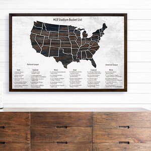 May include: A framed print of a map of the United States with each state shaded in a wood grain pattern. The map is titled "MLB Stadium Bucket List" and lists all the Major League Baseball stadiums by state and city.