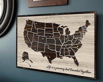 May include: A wooden map of the United States with a white background and a dark brown wood grain finish. The map is divided into states and has gold pins in each state. The text "Life is a journey best traveled together" is written at the bottom of the map.