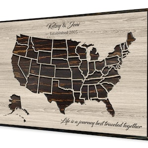 May include: A wooden wall art piece featuring a map of the United States with each state outlined. The map is dark brown with a light wood background. The text "Kelsey & Jeni - Established 2005 - Life is a journey best traveled together" is printed below the map.