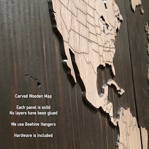 K&ouml;nnte beinhalten: Eine geschnitzte Weltkarte aus Holz mit einer dunkelbraunen Beize. Die Karte besteht aus zwei Teilen, einer zeigt Nord- und S&uuml;damerika und der andere Europa, Afrika, Asien und Australien. Der Text "Carved Wooden Map" ist am unteren Rand des Bildes sichtbar. Der Text "Each panel is solid" ist unter der Karte sichtbar. Der Text "No layers have been glued" ist unter dem vorherigen Text sichtbar. Der Text "We use Beehive Hangers" ist unter dem vorherigen Text sichtbar. Der Text "Hardware is included" ist unter dem vorherigen Text sichtbar.