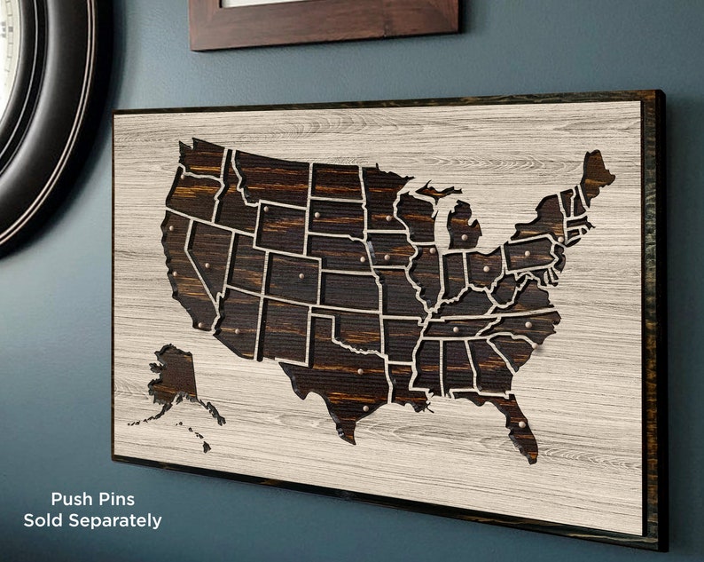 May include: A wooden map of the United States with each state outlined. The map is on a whitewashed wood background with a dark wood frame. The text "Push Pins Sold Separately" is at the bottom of the image.