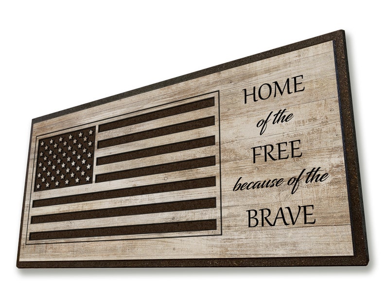 May include: A wooden doormat with a brown woodgrain pattern and a black border. The doormat features a cutout of the American flag and the text "HOME of the FREE because of the BRAVE".