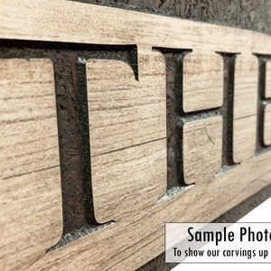 May include: Close-up of a wooden sign with the word "THE" carved into it. The letters are black and the wood is a light brown color. The sign is a sample photo to show the detail of the carving.