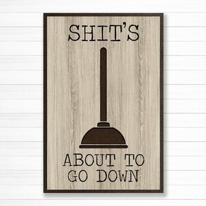 May include: A brown wooden sign with a black outline and the text "SHIT'S ABOUT TO GO DOWN" with a black silhouette of a plunger in the middle.