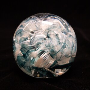 May include: A glass paperweight with swirling blue and white patterns inside. The glass is clear and the patterns are abstract.