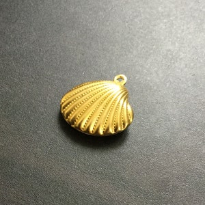 Op de afbeelding: Een gouden schelp hanger met een getextureerd oppervlak.