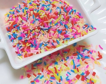 May include: A white bowl filled with colorful sprinkles. The sprinkles are long and thin, and they are in a variety of colors, including red, orange, yellow, green, blue, and purple.