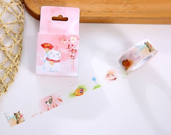 May include: A roll of decorative washi tape with a white background and colorful illustrations of cats and flowers. The tape is packaged in a small pink box with a cat illustration and the text "上  店  好  运" in Chinese characters.