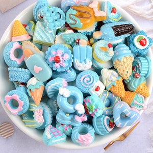 May include: A collection of blue and white miniature cake and ice cream charms. The charms are decorated with sprinkles, frosting, and other details.