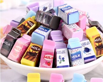 Könnte beinhalten: Eine Schüssel gefüllt mit bunten Radiergummis in Form von Milchpackungen. Die Radiergummis haben verschiedene Designs, darunter Schokoladenmilch, Erdbeermilch, Blaubeermilch und eine Milchpackung mit dem Wort "LOVE" darauf.