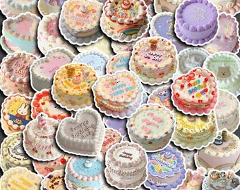 May include: A selection of small, decorated cakes in various shapes and colours. Some cakes are heart-shaped, others round, and some have text like "Happy Birthday" and "Happy Day". The cakes feature pastel colours and decorative icing.